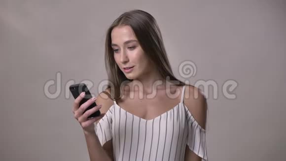 年轻兴奋的女孩正在展示绿色的智能手机屏幕看着相机微笑交流理念灰色视频的预览图