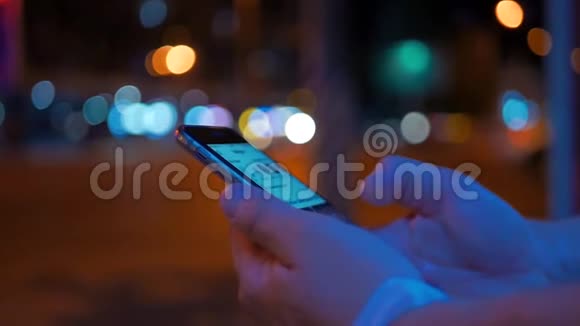 一名男子晚上在路边使用智能手机的特写镜头彩色模糊的城市和红绿灯视频的预览图