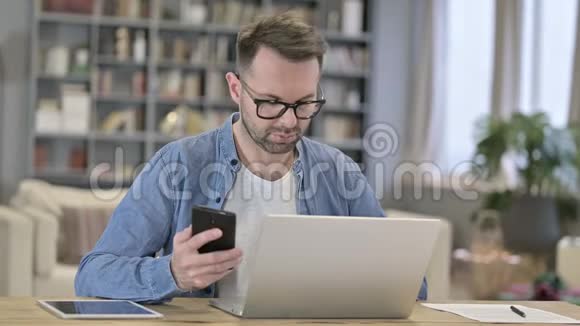 年轻人在智能手机上说话在笔记本电脑上工作视频的预览图