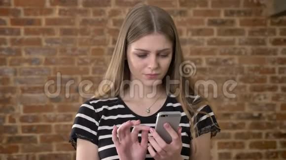 年轻可爱的金发女郎正在智能手机上输入信息微笑交流理念砖背景视频的预览图