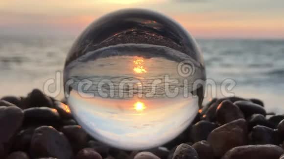 水晶球内美丽的背景景观镶嵌在沙滩上的石头夕阳和海浪中视频的预览图