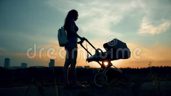 日落时分美丽的女人带着婴儿车在城市公园散步视频的预览图