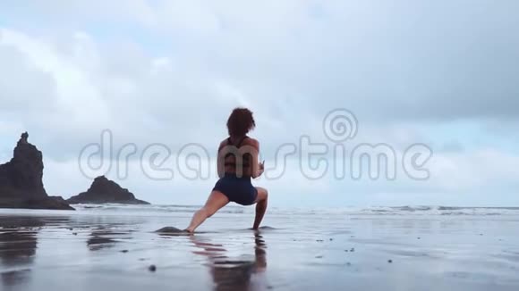 快乐的年轻女子在日落时在海滩上练习瑜伽健康活跃的生活方式理念慢动作视频的预览图