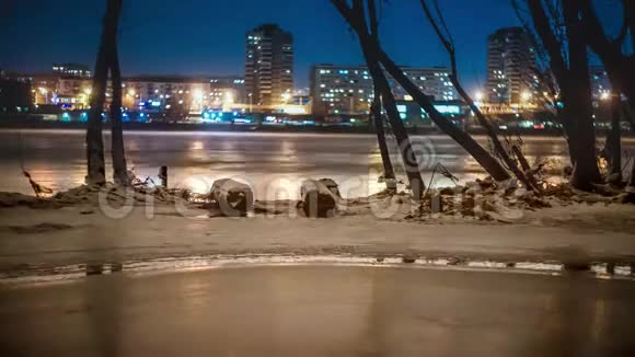 冬天解冻的河流在冰的岸边树木的轮廓背景是夜城的灯火视频的预览图
