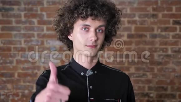 年轻的白种人卷发竖起大拇指对着镜头微笑自信的男性砖墙背景视频的预览图