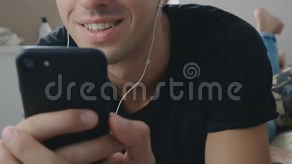年轻人躺在明亮的客厅里带着耳机一边听音乐一边用智能手机视频的预览图