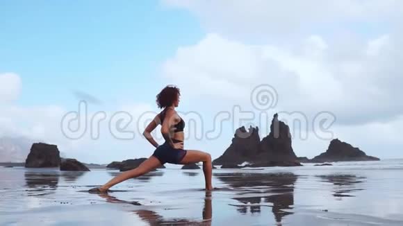 快乐的年轻女子在日落时在海滩上练习瑜伽健康活跃的生活方式理念慢动作视频的预览图