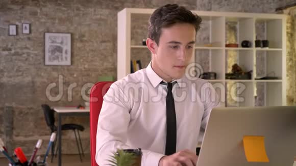 年轻的快乐商人在办公室里拿着笔记本电脑喝着咖啡看着镜头商业理念视频的预览图