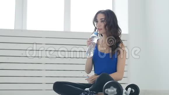 年轻女子在健身房训练常规后放松在室内用饮用水重新调节自己视频的预览图