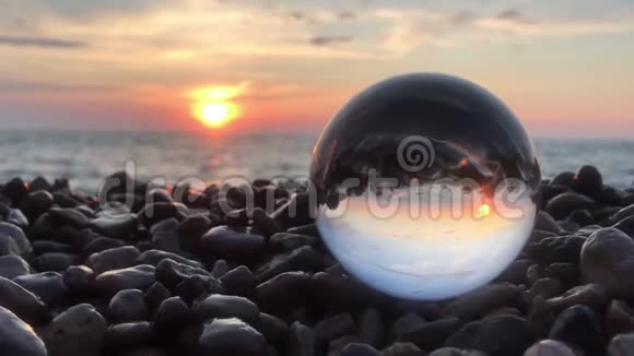 水晶球内美丽的背景景观镶嵌在沙滩上的石头夕阳和海浪中视频的预览图