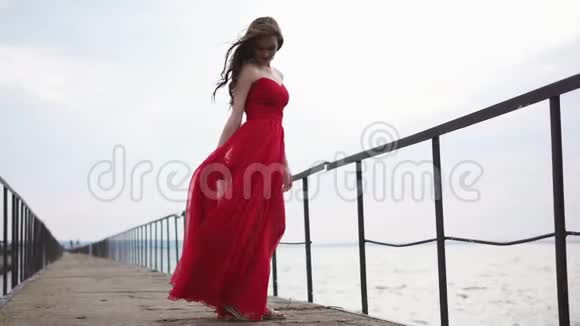 穿着红色衣服的年轻女子站在靠近大海的桥上视频的预览图