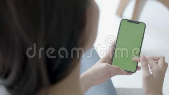 亚洲女人手牵着手看着用绿色屏幕的智能手机在沙发上自己定制内容视频的预览图