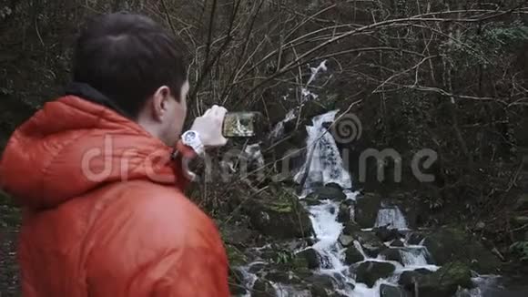 男子通过电话在林地拍摄小溪流的后景视频的预览图