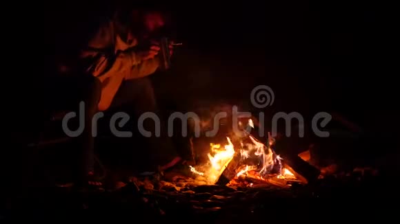 大胡子的男人喝着大杯子里的茶在黑暗中在篝火的手机上拍张照片4K视频的预览图