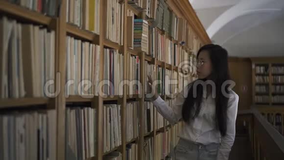 年轻迷人的女人正在室内沿着大学图书馆散步视频的预览图