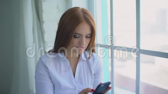年轻的微笑的女人拨了一个号码坐在家附近的一扇窗户上开始打电话慢动作视频的预览图