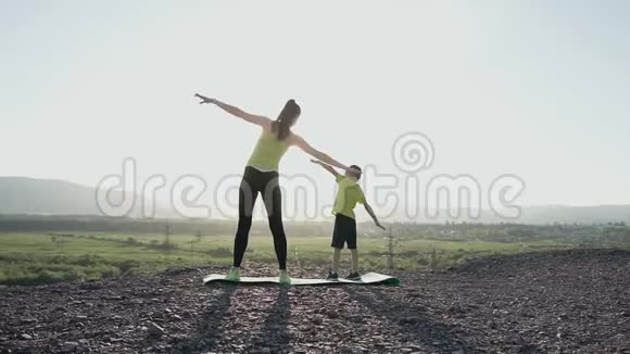 日落或日出时母亲和儿子在山顶上做运动锻炼的后景运动员家属姐妹视频的预览图