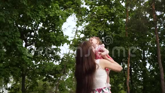 当她在空中飞翔时女孩在妈妈的怀里笑妈妈抱着快乐的婴儿在绿色公园散步产妇视频的预览图