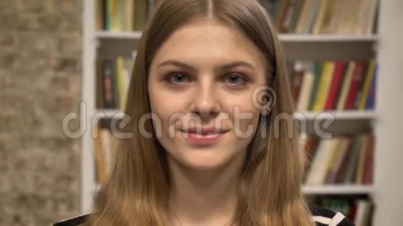 年轻可爱的金发女郎正在镜头前看着微笑着在后台看图书馆视频的预览图