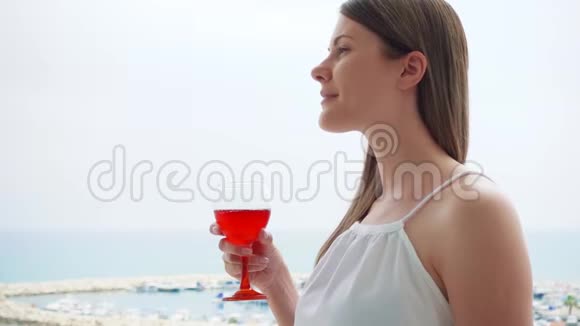 女人从阳台上欣赏海景度假女性在阳台上慢悠悠地喝玫瑰酒视频的预览图