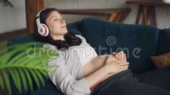 期待着母亲在沙发上放松用耳机听音乐用爱和关怀抚摸她的肚子视频的预览图