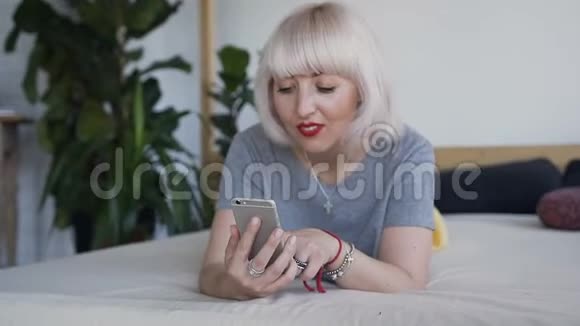 一个长着雀斑的金发女人躺在大床上微笑着看着电话视频的预览图