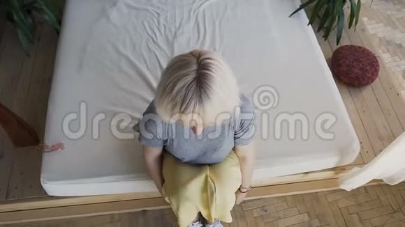 俯视美丽的金发女郎躺在大床上打断了她的手臂一个在白色床上对着背景微笑的女孩视频的预览图