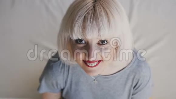 合拢美丽的金发女郎的乐趣躺在大床上打断她的手臂在白色床上微笑的女人反对这个概念视频的预览图