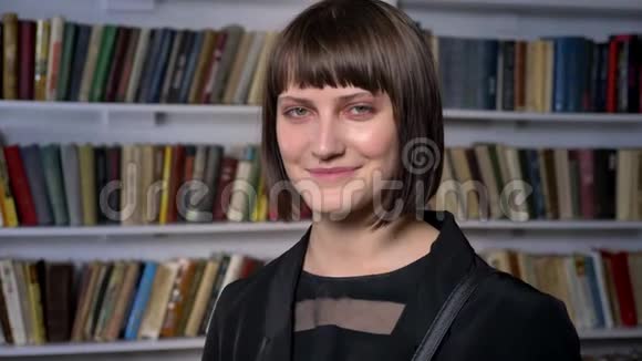 年轻快乐的迷人女子短发站在图书馆对着镜头微笑笑着视频的预览图