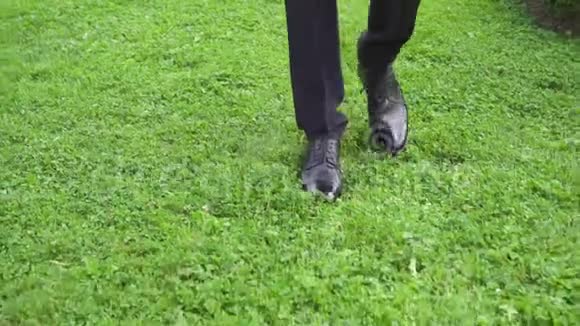穿着时髦鞋子走在绿草上的男商人的脚视频的预览图