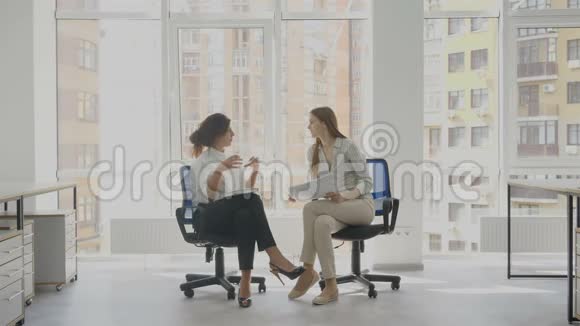 办公室工作人员两个女人坐在椅子上交谈讨论工作文件公司事务其中之一视频的预览图