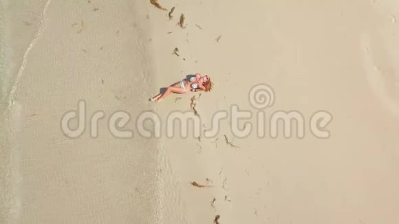 美丽的女人穿着比基尼躺在沙滩上的沙滩上鸟瞰夏天海滩海浪和沙滩上晒黑的女人视频的预览图
