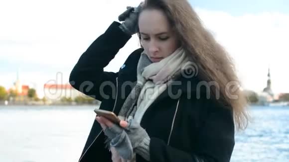 漂亮的女孩留着漂亮的长发发短信在户外使用手机智能手机背景是老城视频的预览图