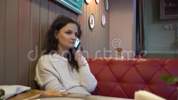 年轻的女人在电话里说话微笑地看着相机在咖啡馆里休息视频的预览图