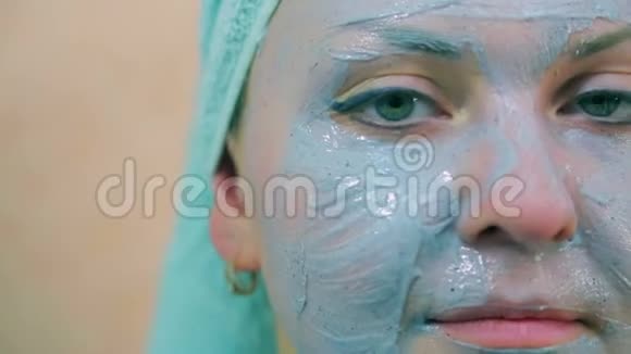 一个微笑的女人的脸头上有一条毛巾皮肤上有一刷蓝色的粘土特写镜头在看着视频的预览图