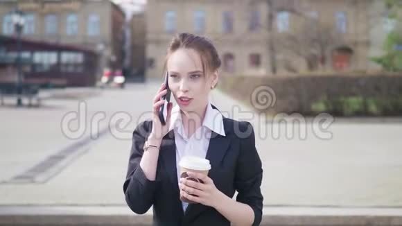 一位年轻漂亮的商业女学生穿着西装在城市里走来走去喝着咖啡谈论着视频的预览图