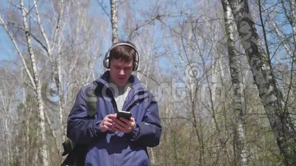 一个年轻人走在公园里通过耳机听音乐早晨在春天的新鲜空气中散步视频的预览图