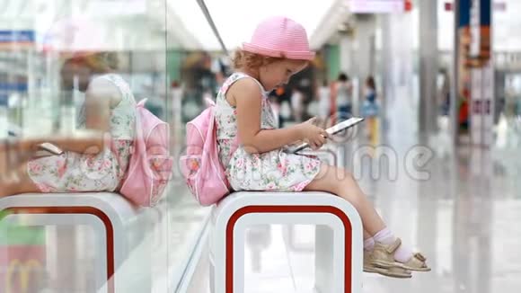 小女孩坐在购物中心玩平板电脑婴儿在智能手机上使用游戏应用程序视频的预览图