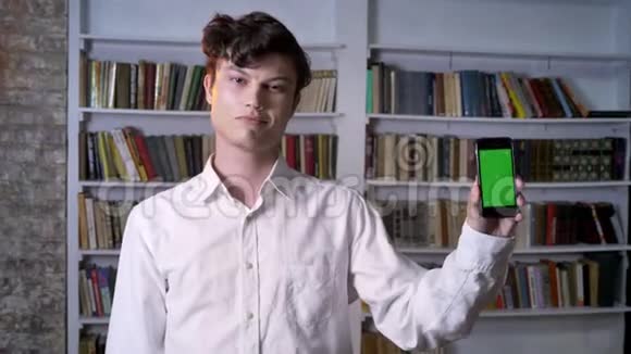 布鲁内特曼正在展示智能手机的绿色屏幕在镜头下观看交流概念背景图书馆视频的预览图