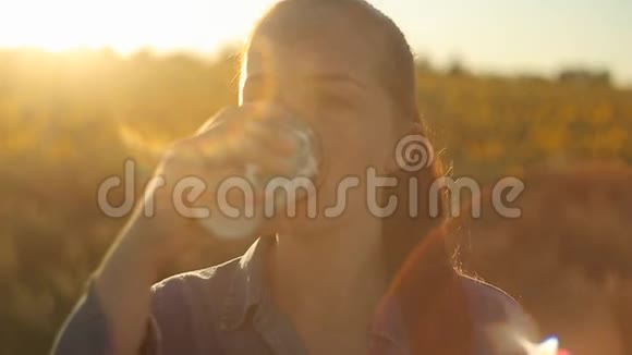 傍晚夕阳西下红发的年轻美女在向日葵的田野里喝咖啡视频的预览图