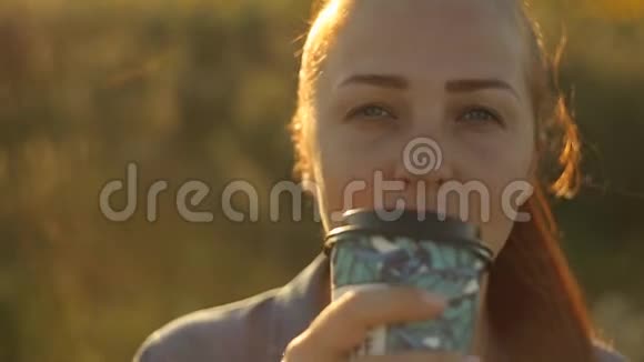 傍晚夕阳西下红发的年轻美女在向日葵的田野里喝咖啡视频的预览图