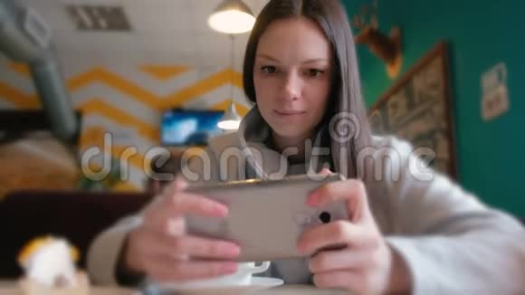 年轻女子黑发正在咖啡馆里玩手机视频的预览图
