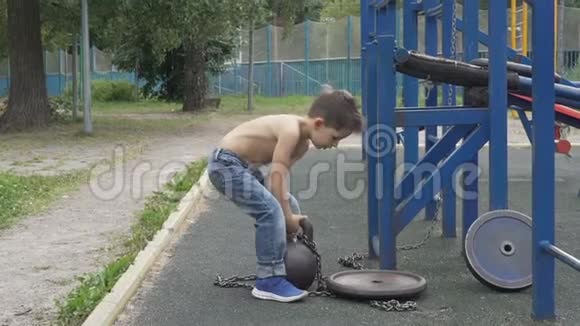 小男孩在户外运动场上举起沉重的水壶铃视频的预览图