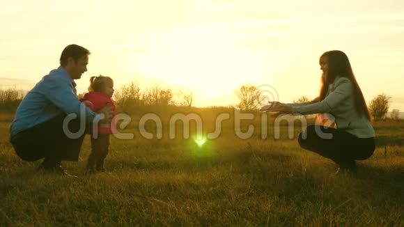 爸爸妈妈和孩子在日落时在草地上玩家庭幸福的概念宝宝从爸爸到妈妈都在草坪上儿童视频的预览图
