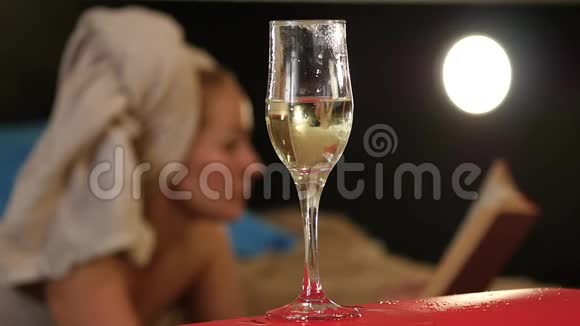 特写香槟流入玻璃杯中美丽的女人躺在床上看书慢动作视频的预览图