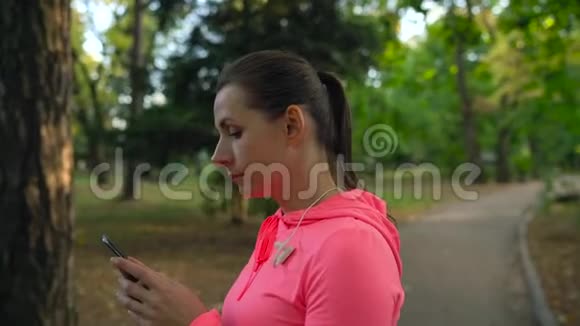 带无线耳机和智能手机的女人选择音乐穿过秋天的公园慢动作视频的预览图