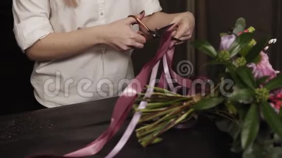 一个穿着白色衬衫的女孩剪下粉红色的长丝带和紫色的宽丝带装饰一束鲜花视频的预览图