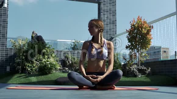女孩坐在瑜伽姿势的休息露台与草坪视频的预览图
