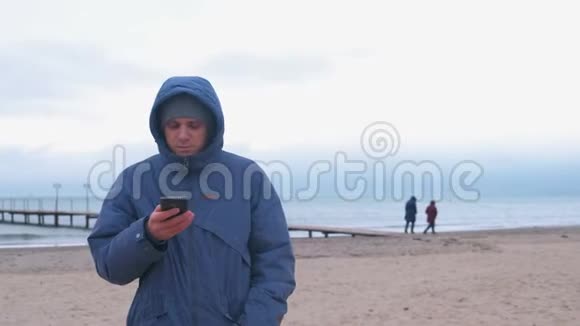 冬天穿着夹克的人在海边的海边玩手机视频的预览图