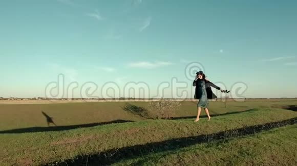 快乐的女孩戴着帽子赤脚在秋天阳光明媚的日子里在草原的中间奔跑视频的预览图